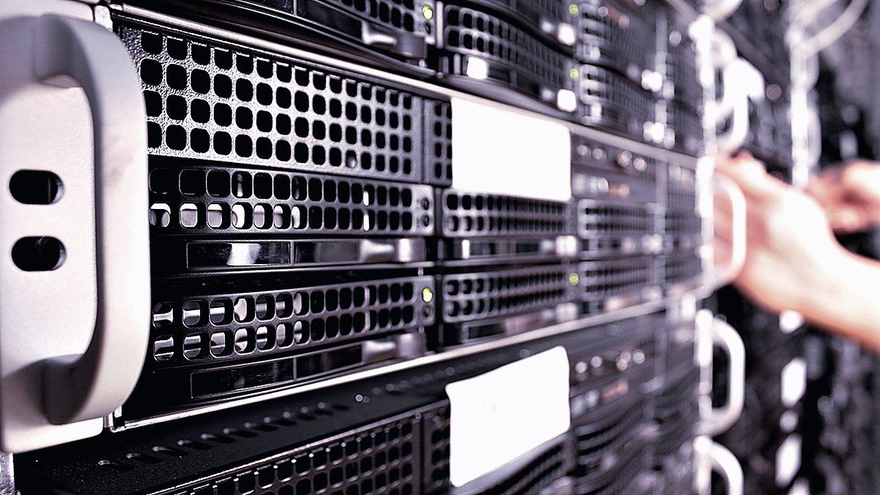 Close-up van serverkasten in een rek in een datacenter, met op de achtergrond een onscherpe hand bij een handgreep