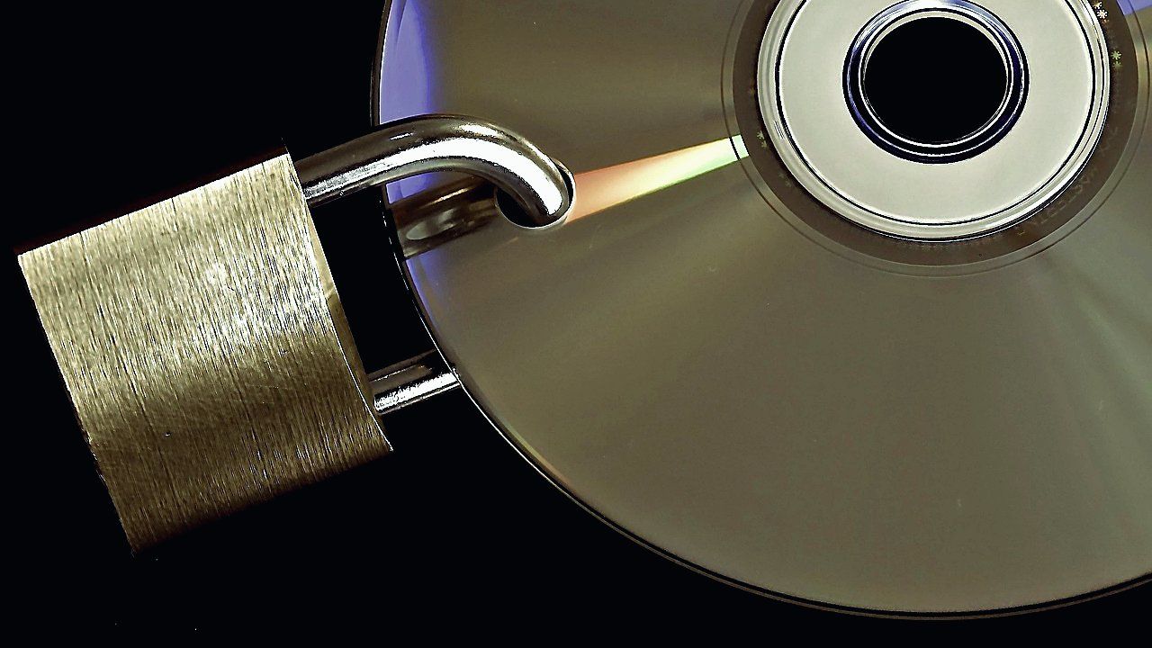 Metalen hangslot met de beugel door het gat van een glanzende cd of dvd, tegen een zwarte achtergrond