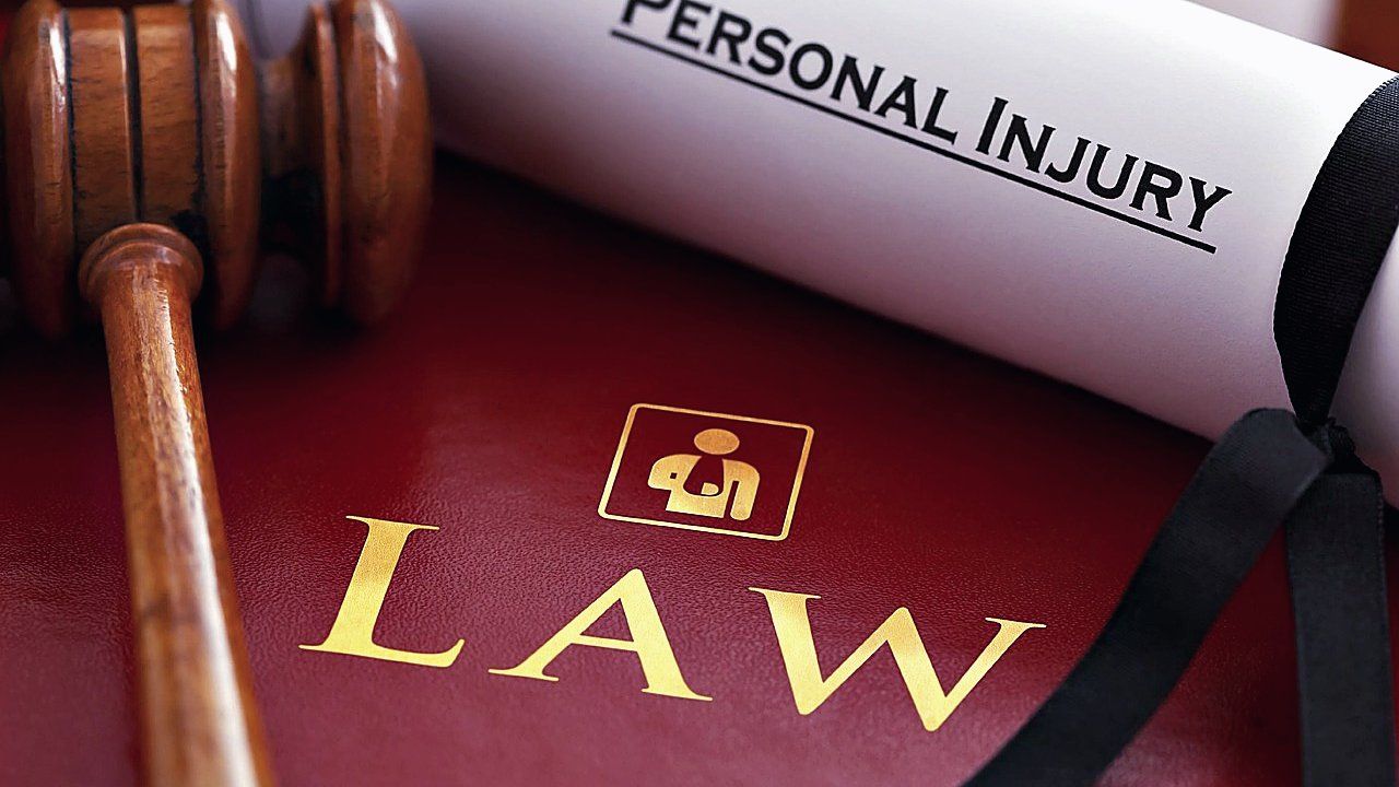 Houten hamer naast een rode wetboekband met gouden tekst LAW en een opgerolde akte met opschrift Personal Injury