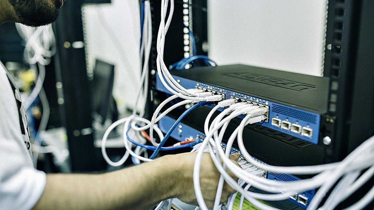 Man in wit shirt sluit witte netwerkkabels aan op een zwarte switch in een serverrek